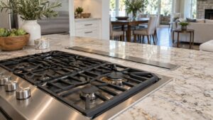 A stainless downdraft unit retracted flush behind a cooktop in a kitchen island with stone counter