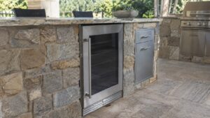 A built-in stainless steel outdoor beverage center set into a stone kitchen island, matched precisely to the surrounding countertop cutout
