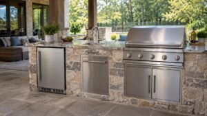 An outdoor beverage center built into a stone patio island next to a built-in grill