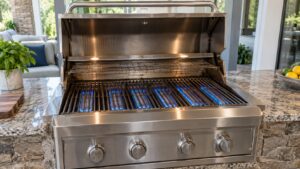 A stainless steel built-in gas grill with its hood fully open and bright blue flames burning evenly under the grates