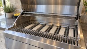 The open hood of a built-in stainless gas grill showing rows of ceramic rods over the burners, no text or labels