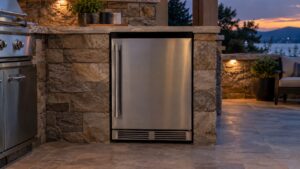 A built-in stainless steel outdoor refrigerator with a completely dark control panel in an outdoor kitchen at dusk, no text or labels